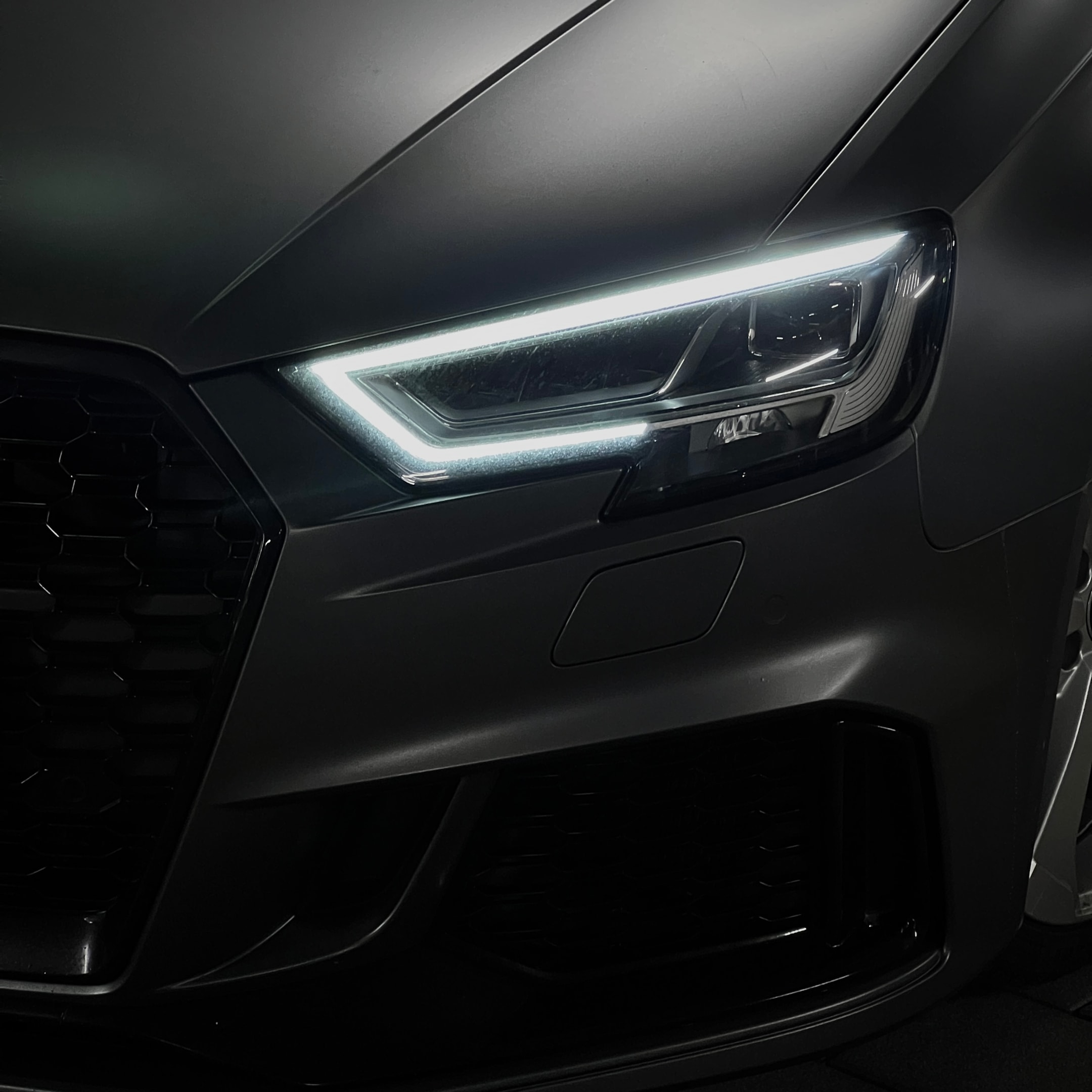 Detailaufnahme der Front eines Audi RS3 mit markantem LED-Scheinwerfer und mattem Finish – sportliches Design eines Performance-Fahrzeugs für exklusive Sportwagenmiete über die Drivable App.