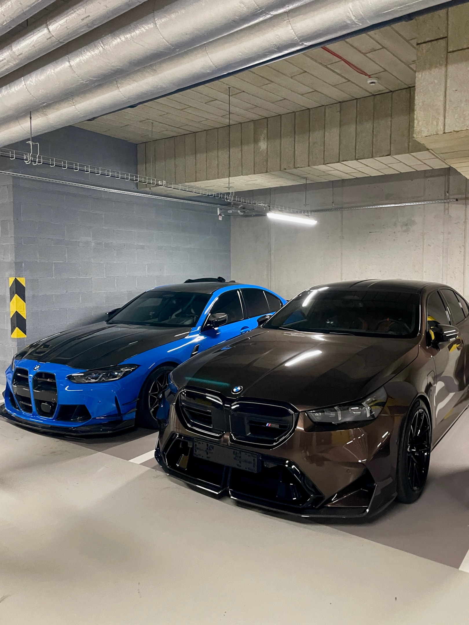 Zwei BMW M-Modelle in moderner Tiefgarage – BMW M4 und BMW M3 als leistungsstarke Sportlimousinen, ideal für exklusive Sportwagenmiete und Performance-Erlebnisse über die Drivable App.